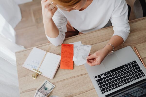 Cô gái trẻ ngồi bàn làm việc, xem hóa đơn và ghi chép kế hoạch chi tiêu cá nhân